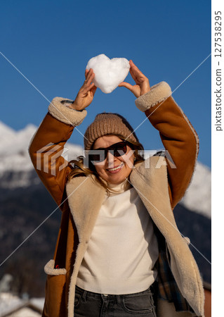 Snow Heart Mountains Woman Winter: Happy woman holding snow heart, sunny mountain winter day, joyful outdoor activity. 127538295