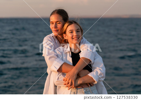 Mother Daughter Beach Sunset - Two women embrace while looking out at the ocean during a sunset. Mother Daughter Beach Sunset - Two women embrace while looking out at the ocean during a sunset. 127538330