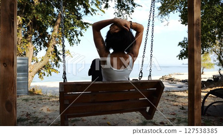 Happy woman ride on swing at tropical at sea beach. Carefree lady enjoying rest near ocean. Adult female having fun at sea shore on sunny day. Concept of summer vacation or holiday. Slow motion 127538385