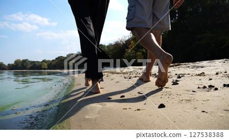 Bare feet of couple stepping together along sand beach at coastline. Male and female legs of pair walking near seaside. Happy lovers going along sandy shore. Concept of summer vacation or holiday 127538388