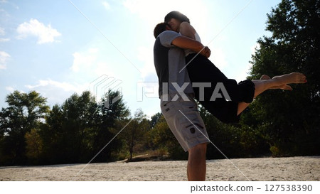 Happy couple having fun together on seashore at summer vacation. Man taking woman in air and turning around at coastline. Carefree lovers spending time at sandy beach. Concept of love. Slow motion 127538390