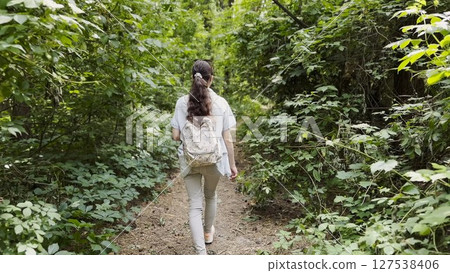 Young woman going along path at summer forest. Female with backpack walking among trail at wild nature. Unrecognizable girl enjoying stroll outdoor admiring beautiful scenic. Close up Rear view Young woman going along path at summer forest. Female with backpack walking among trail at wild nature. Unrecognizable girl enjoying stroll outdoor admiring beautiful scenic. Close up Rear view 127538406
