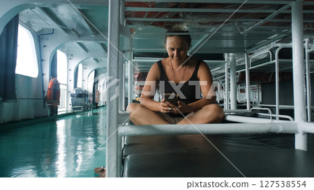 Inside a ferry cabin, a woman relaxes on a bed, scrolling through her phone on the journey Inside a ferry cabin, a woman relaxes on a bed, scrolling through her phone on the journey 127538554