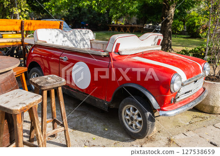 Retro red convertible car repurposed as outdoor seating. Vintage automotive decor, upcycled design and quirky cafe atmosphere. Retro red convertible car repurposed as outdoor seating. Vintage automotive decor, upcycled design and quirky cafe atmosphere. 127538659