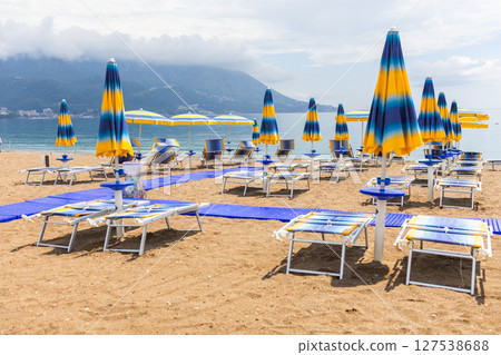 Tranquil morning at a beach with blue umbrellas and loungers. Coastal vacation, summer relaxation and peaceful seaside tourism. 127538688