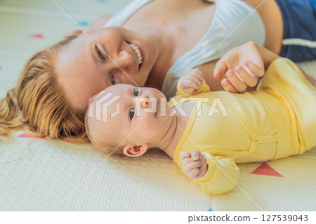 Mother and baby lying on a play mat. Tender bonding moment, cozy childhood atmosphere, and early development. Parenting, love, and infant care concept 127539043