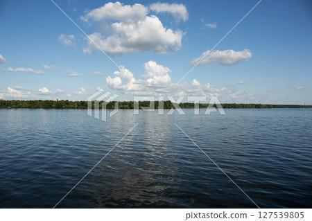 Panoramic view of the Dnieper river bank from the embankment of city of Dnieper. Reflection of the sky with clouds on the surface of the water. 127539805