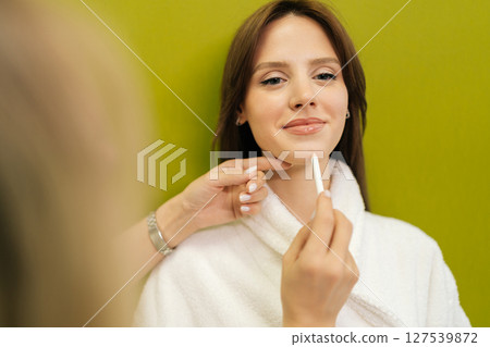 View from shoulder of beautician marking facial contours with pencil, preparing cosmetic procedure on green background. Concept of non-surgery cosmetology, professional skincare, beauty treatment. 127539872