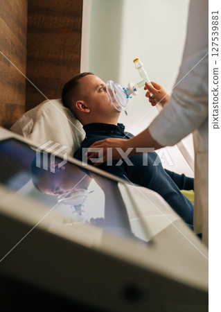 Vertical shot of unrecognizable female doctor assisting to male patient undergoing respiratory training with oxygen mask, providing essential care and monitoring progress in modern medical clinic. 127539881