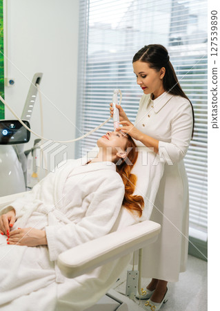 Vertical shot of skilled beautician doctor performing mesotherapy procedure on woman forehead, targeting skin rejuvenation and reducing wrinkles in cosmetology clinic. Concept of beauty treatment. Vertical shot of skilled beautician doctor performing mesotherapy procedure on woman forehead, targeting skin rejuvenation and reducing wrinkles in cosmetology clinic. Concept of beauty treatment. 127539890