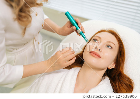 Top view portrait of redhead female receiving rejuvenation treatment in cosmetology clinic. Professional beautician performing mesotherapy treatment to woman focusing on skin rejuvenation, hydration 127539900