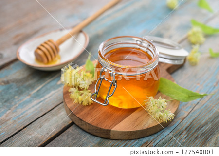Linden honey in glass jar with wooden honey dipper Linden honey in glass jar with wooden honey dipper 127540001