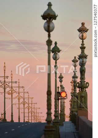rows of lampposts and poles with electric grids for a tram on an empty Troitskiy Bridge at a pink sunset, nobody rows of lampposts and poles with electric grids for a tram on an empty Troitskiy Bridge at a pink sunset, nobody 127540377