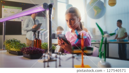 Talented Girl Sitting at Table and Using Smartphone, Conducting Biology Experiment on Plants 127540571