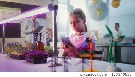 Talented Girl Sitting at Table and Using Smartphone, Conducting Biology Experiment on Plants 127540633