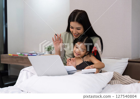 Work from home, freelance and lifestyle concept. Portrait of creative asian female sitting on bed with laptop and her take care of her kid while working 127540804