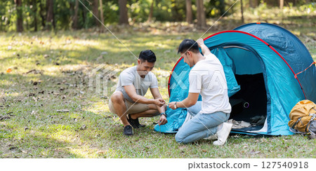 LGBTQIA Gay couple camping together in woods for holidays and helping set up a tent together LGBTQIA Gay couple camping together in woods for holidays and helping set up a tent together 127540918