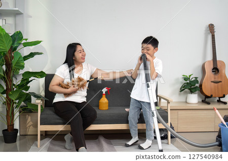 Cleaning and Family Interaction. A mother and son share a light moment while cleaning the living room. 127540984