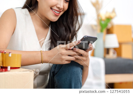 Digital Connection. Young woman using her smartphone while surrounded by moving boxes. Digital Connection. Young woman using her smartphone while surrounded by moving boxes. 127541055