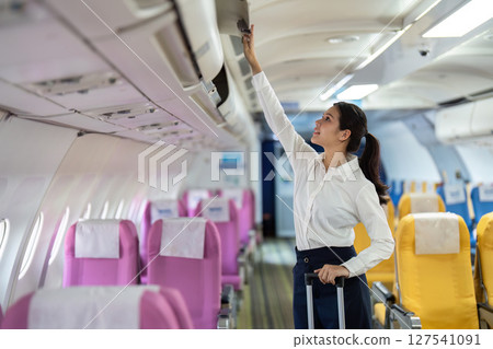 Business travel and organization. A woman reaching for her luggage in an airplane compartment. 127541091