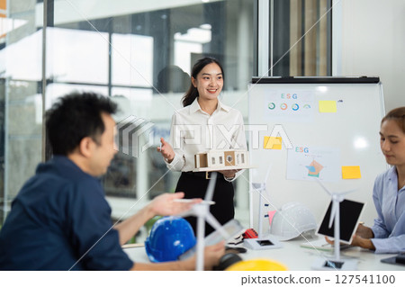 Sustainable Engineering. Female engineer presenting ESG project with model in modern office. Sustainable Engineering. Female engineer presenting ESG project with model in modern office. 127541100