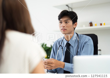 Patient Consultation. A doctor discussing health concerns with a patient in a clinical setting. Patient Consultation. A doctor discussing health concerns with a patient in a clinical setting. 127541115
