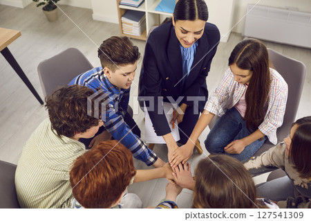 Happy classmates and teacher putting their hands on top of each other Happy classmates and teacher putting their hands on top of each other 127541309