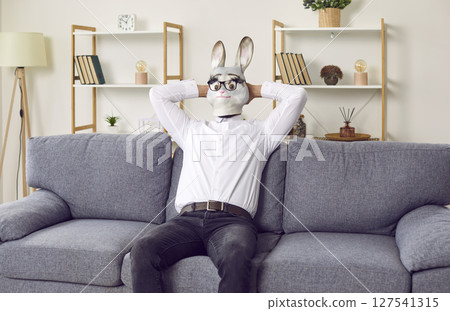 Business man in funny rabbit mask enjoying weekend, sitting on sofa and relaxing 127541315