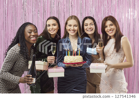 Happy woman holding birthday cake with friends holding glasses of champagne on festive background Happy woman holding birthday cake with friends holding glasses of champagne on festive background 127541346