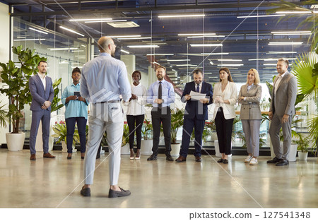 Diverse team of company employees standing in row, listening to business leader or coach on meeting. 127541348