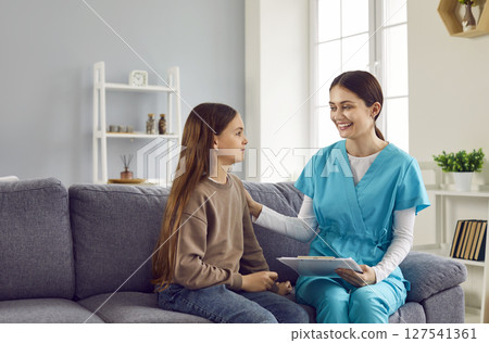 Portrait of friendly nurse supporting sick child girl patient sitting on sofa at home. Portrait of friendly nurse supporting sick child girl patient sitting on sofa at home. 127541361