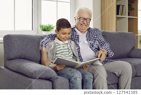 A happy grandpa and his grandson sitting on the sofa and reading a book together A happy grandpa and his grandson sitting on the sofa and reading a book together 127541385
