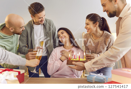 Happy friends congratulating a young smiling girl on her birthday giving her cake at home party Happy friends congratulating a young smiling girl on her birthday giving her cake at home party 127541417
