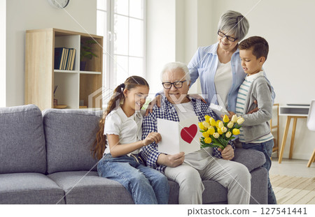 Happy grandfather receives a greeting card and a bouquet of flowers from his family Happy grandfather receives a greeting card and a bouquet of flowers from his family 127541441