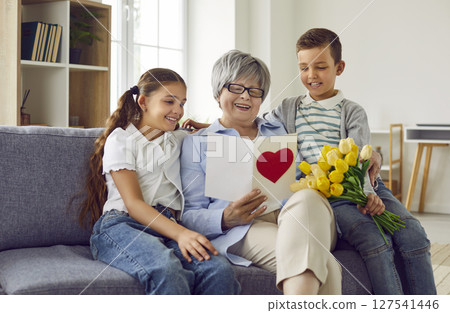 Happy grandmother receives a gift card and a bouquet of flowers from her grandchildren Happy grandmother receives a gift card and a bouquet of flowers from her grandchildren 127541446