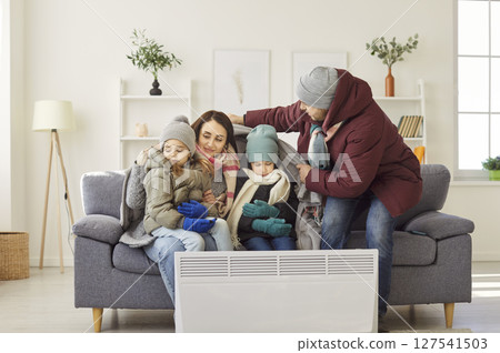 Family Keeping Warm By Heater During Winter At Home 127541503
