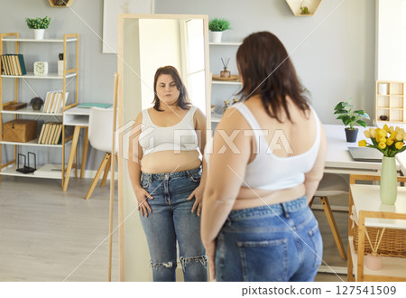 Unhappy plus size woman looking at her reflection in mirror Unhappy plus size woman looking at her reflection in mirror 127541509