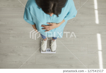 Young expectant mother stands on scales and looks how much weight she has gained 127541517