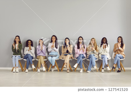 Group of happy diverse business women sitting on chairs in a row on grey wall background on meeting 127541520