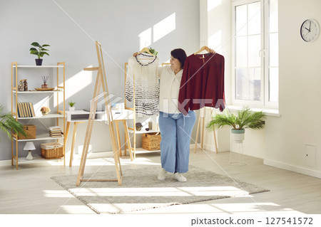 Happy plus size lady looking in mirror and choosing between two different casual tops Happy plus size lady looking in mirror and choosing between two different casual tops 127541572