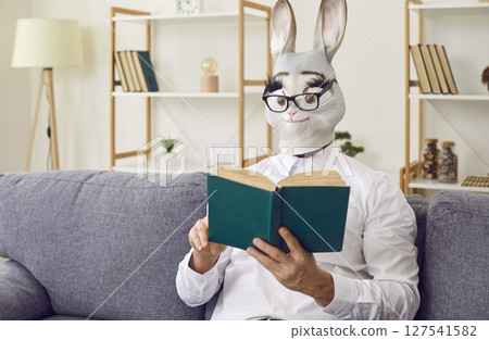Strange man wearing a funny rabbit mask is sitting on the couch and reading a book Strange man wearing a funny rabbit mask is sitting on the couch and reading a book 127541582
