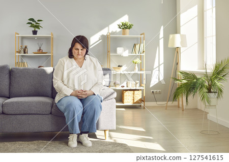 Depressed overweight woman sitting on sofa at home Depressed overweight woman sitting on sofa at home 127541615