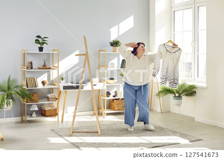 Fat woman dancing in the living room at home with a small size dress dreaming of losing weight. 127541673