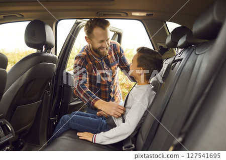 Happy father helps his little son to buckle up before going on road trip together Happy father helps his little son to buckle up before going on road trip together 127541695