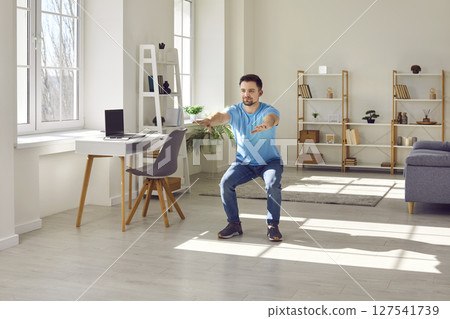 Fit young man doing squatting exercise during a fitness workout in the living room 127541739
