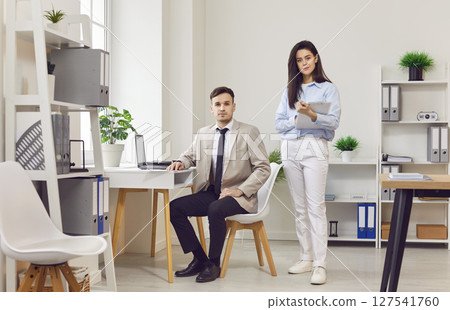 Young positive business office male, female colleagues posing at desk as team in coworking area Young positive business office male, female colleagues posing at desk as team in coworking area 127541760