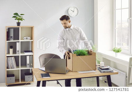 Sad fired dismissed employee with moving box of his belongings standing near his workplace. Sad fired dismissed employee with moving box of his belongings standing near his workplace. 127541781