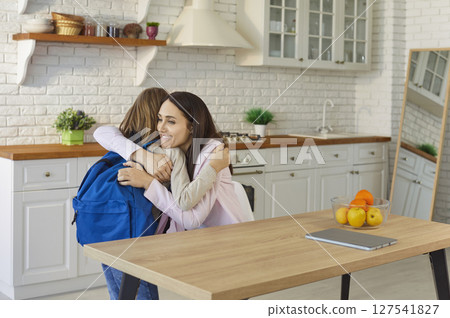 Loving mother giving hug to small pupil child, warm embrace before school day in modern kitchen Loving mother giving hug to small pupil child, warm embrace before school day in modern kitchen 127541827