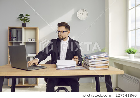 Young business man working at the desk with a pile of documents on his workplace at office. 127541866