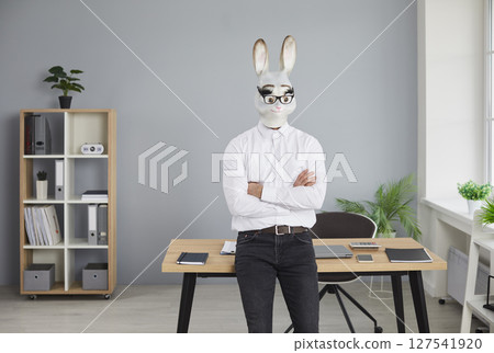Businessman in rabbit head mask standing with folded hands in office 127541920